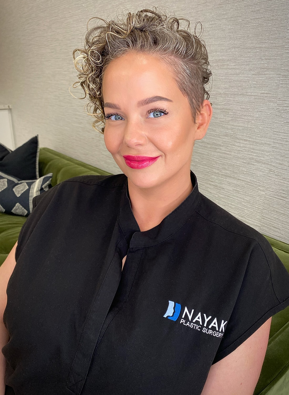 Woman smiling in a black shirt, plastic surgery logo.