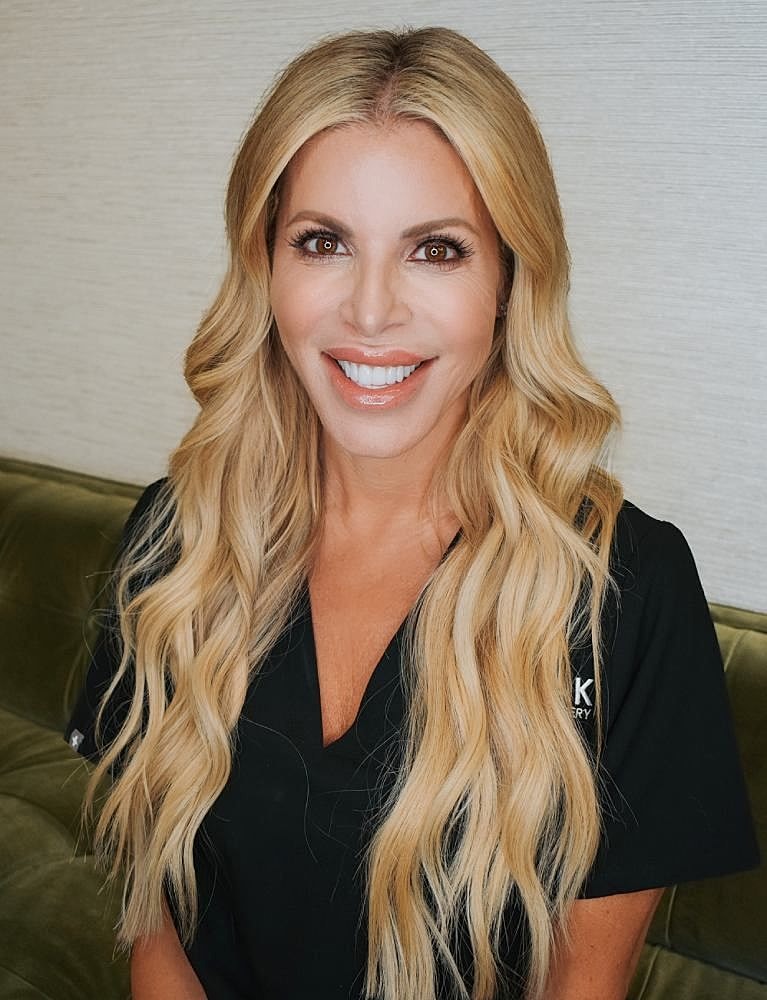 Smiling person in professional attire with wavy hair.