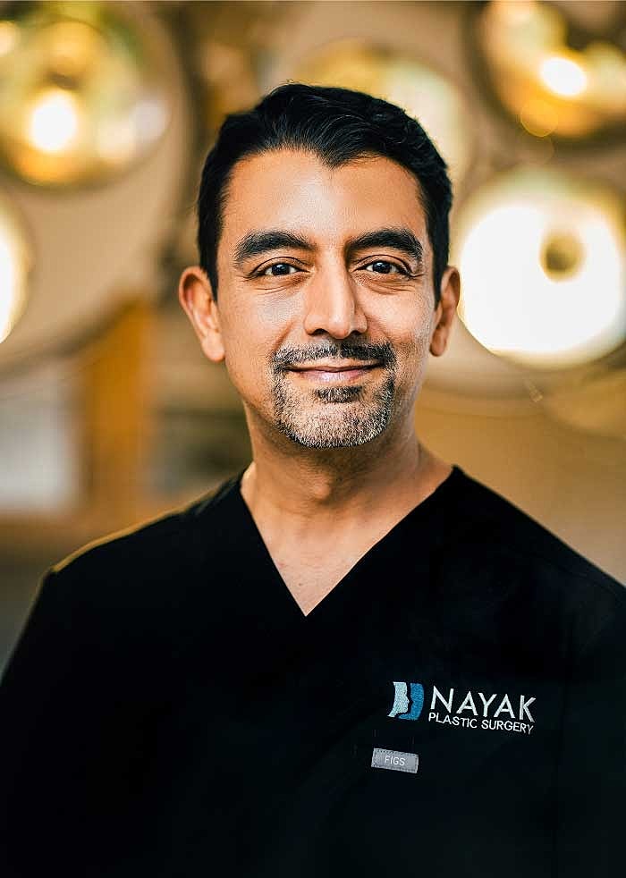 Plastic surgeon smiling in surgical attire.
