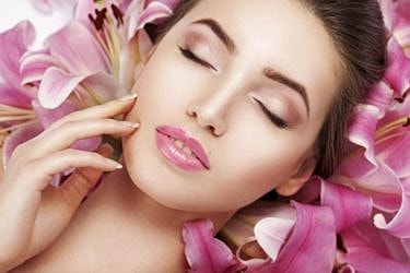 Woman surrounded by pink lilies, serene expression.
