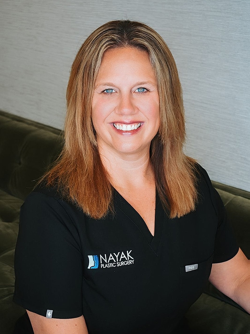 Smiling woman in medical scrubs against a wall.