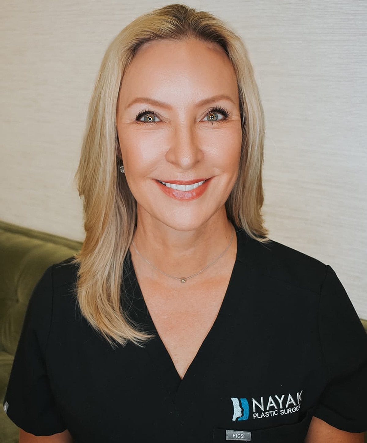 Smiling woman in medical attire at plastic surgery office.
