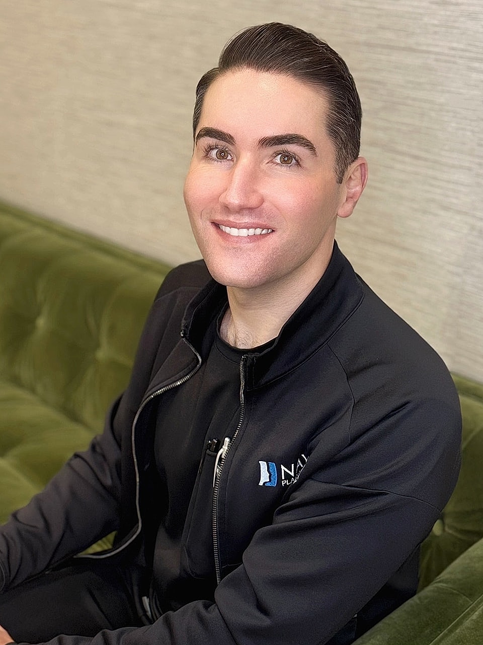 Smiling man in a black jacket, seated.
