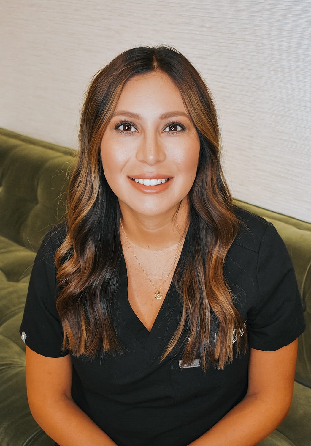 Smiling woman in medical scrubs, seated on couch.